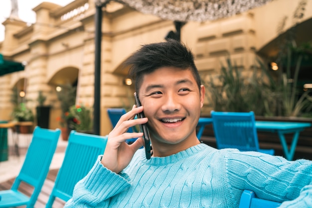 Ritratto di giovane uomo asiatico, parlando al telefono mentre è seduto in una caffetteria.