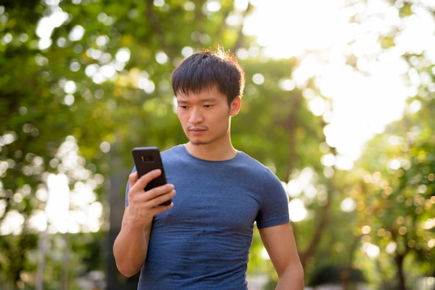 Ritratto di giovane uomo asiatico utilizzando il telefono presso il parco all'aperto