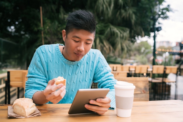 Ritratto di giovane uomo asiatico utilizzando la sua tavoletta digitale mentre è seduto in una caffetteria. Concetto di tecnologia.