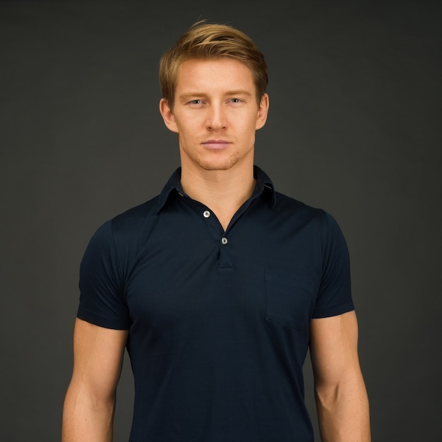 Ritratto di giovane uomo atletico che indossa la maglietta polo blu scuro mentre si trovava sullo spazio grigio