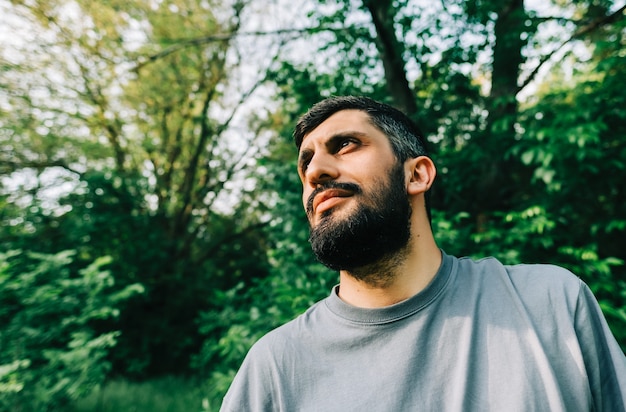 Ritratto di giovane uomo barbuto caucasico all'aperto con sfondo di vegetazione