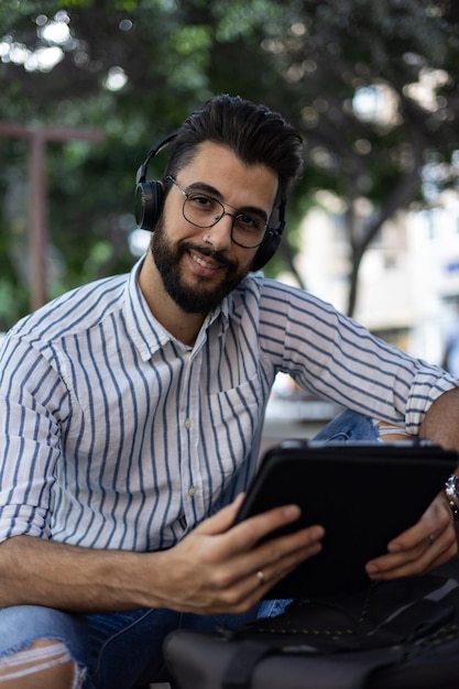 Ritratto di giovane uomo barbuto che guarda l'obbiettivo sorridente con un tablet in mano