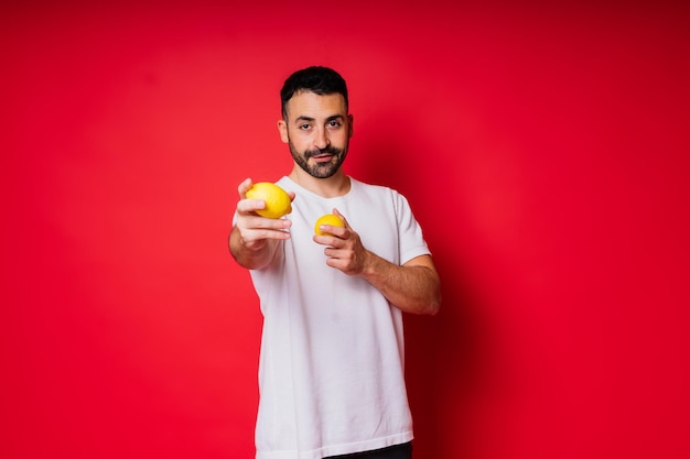 Ritratto di giovane uomo barbuto che tiene i limoni in entrambe le mani su sfondo rosso isolato