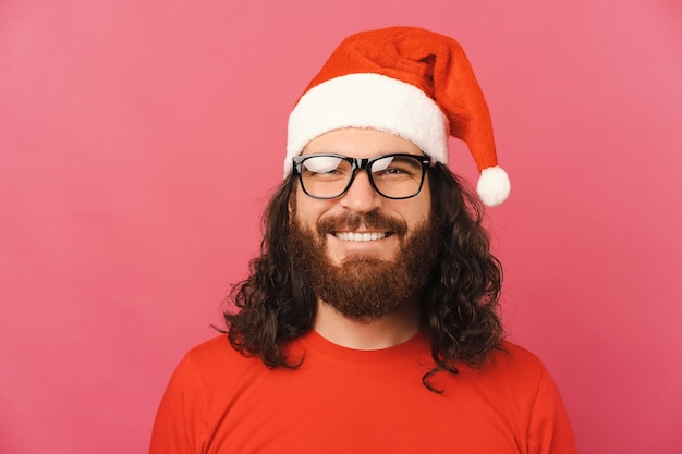 Ritratto di giovane uomo bearde che indossa occhiali e cappello di Babbo Natale su sfondo rosa