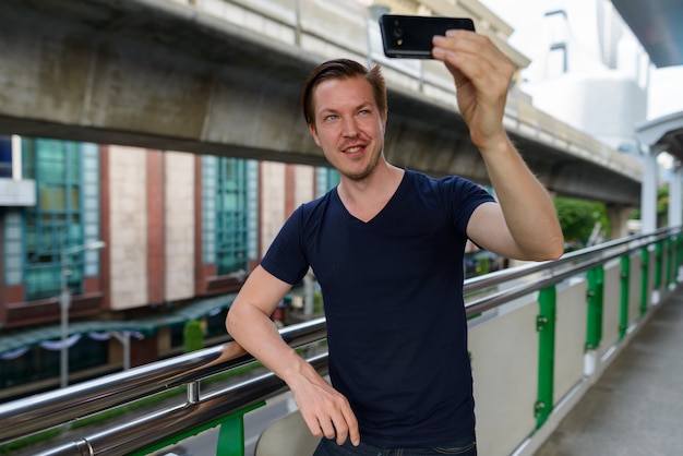 Ritratto di giovane uomo bello alla stazione del treno del cielo in città all'aperto