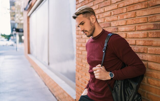 Ritratto di giovane uomo bello che trasporta uno zaino e indossa abiti casual sul muro di mattoni