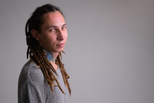 Ritratto di giovane uomo bello con i dreadlocks contro il muro bianco