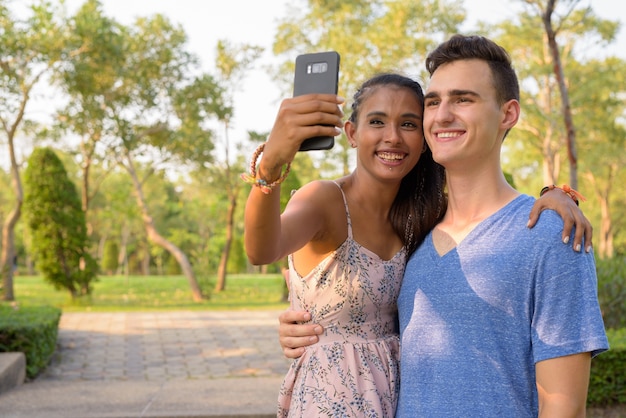 Ritratto di giovane uomo bello e giovane bella donna asiatica rilassante insieme al parco