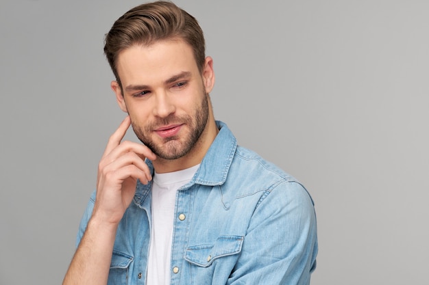 Ritratto di giovane uomo bello in camicia di jeans sopra la parete chiara