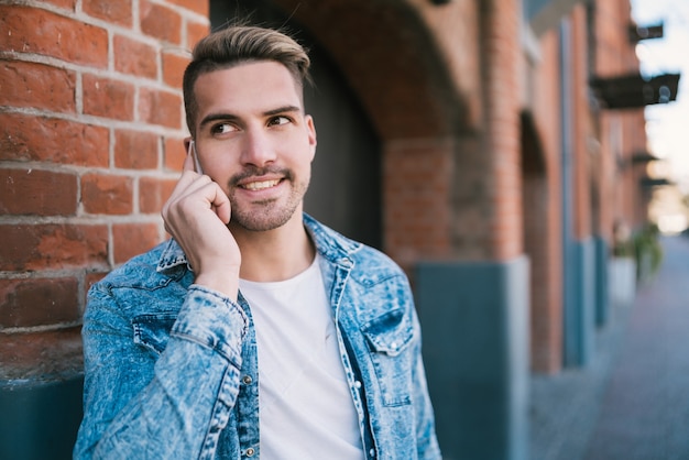 Ritratto di giovane uomo bello parlare al telefono all'aperto in strada. Concetto di comunicazione.