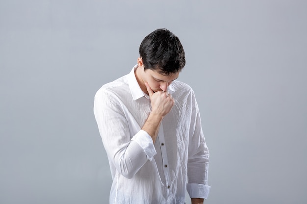 Ritratto di giovane uomo castana pensieroso bello in camicia bianca su fondo grigio.