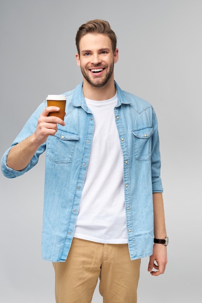 Ritratto di giovane uomo caucasico bello in camicia di jeans che tiene tazza di caffè per andare