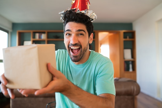 Ritratto di giovane uomo che festeggia il suo compleanno in una videochiamata e apre i regali mentre si resta a casa