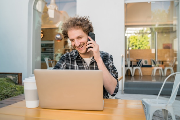 Ritratto di giovane uomo che parla al telefono mentre è seduto in una caffetteria. Concetto di comunicazione.