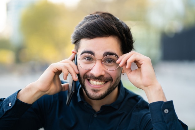 Ritratto di giovane uomo che parla al telefono mentre si sta in piedi all'aperto per strada. Concetto urbano.