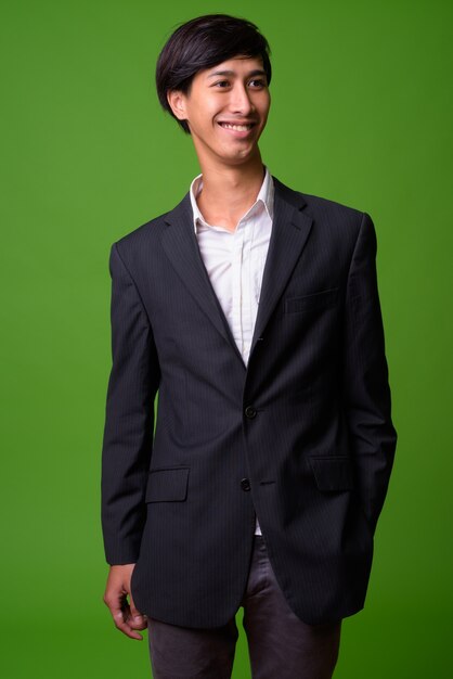 Ritratto di giovane uomo d'affari asiatico contro il muro verde