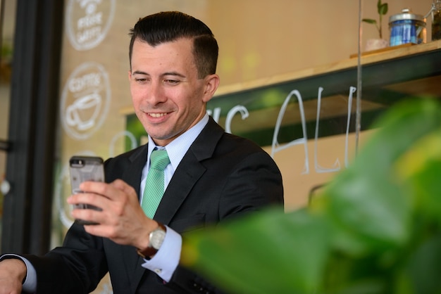 Ritratto di giovane uomo d'affari bello in vestito presso la caffetteria all'aperto