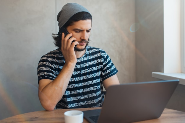 Ritratto di giovane uomo d'affari che ha una conversazione con un'altra persona sullo smartphone mentre si lavora al computer portatile.