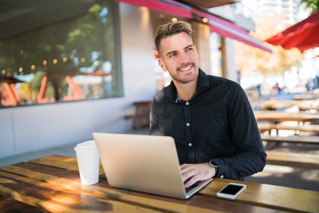 Ritratto di giovane uomo d'affari che lavora al suo computer portatile mentre era seduto in una caffetteria. Tecnologia e concetto di business.