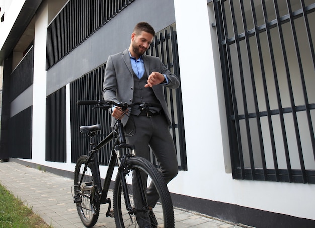 Ritratto di giovane uomo d'affari con la sua bicicletta guardando l'orologio