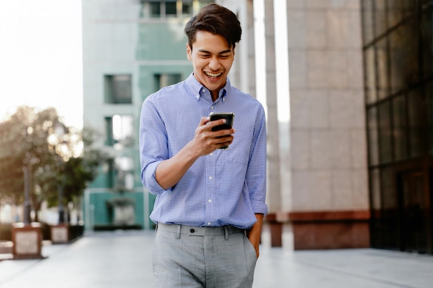 Ritratto di giovane uomo d'affari felice facendo uso del telefono cellulare nella città urbana.
