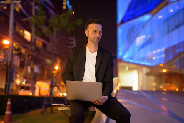 Ritratto di giovane uomo d'affari utilizzando laptop contro una città di notte