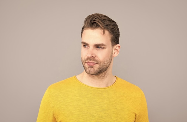 Ritratto di giovane uomo di bell'aspetto con la faccia non rasata in maglione giallo sfondo grigio bello