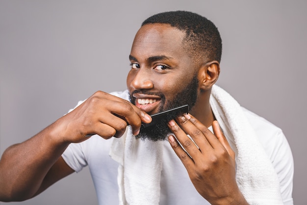 Ritratto di giovane uomo di colore afroamericano bello che pettina la sua barba in bagno. Isolato su sfondo grigio.