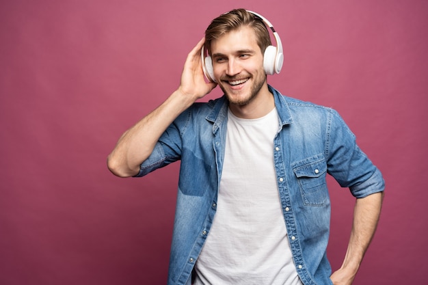 Ritratto di giovane uomo felice che ascolta la musica con le cuffie isolate su sfondo rosa.