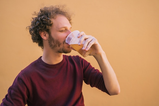 Ritratto di giovane uomo godendo e bevendo birra contro lo spazio giallo. Concetto di stile di vita.