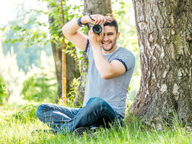 Ritratto di giovane uomo hipster con fotocamera all'aperto Giovane fotografo maschio che fotografa la natura in una giornata estiva