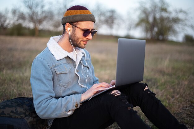 Ritratto di giovane uomo hipster utilizzando laptop all'aperto