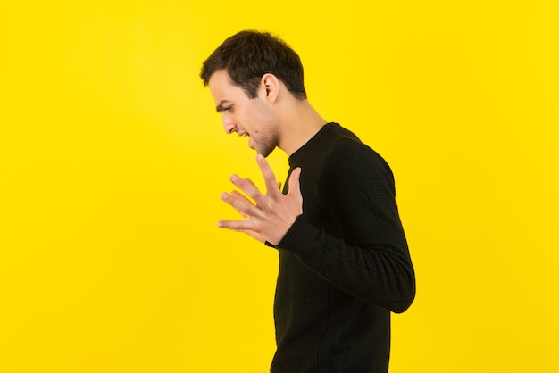 Ritratto di giovane uomo in felpa nera che urla sul muro giallo