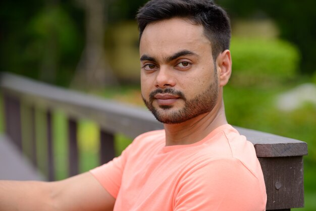 Ritratto di giovane uomo indiano barbuto bello presso il parco all'aperto