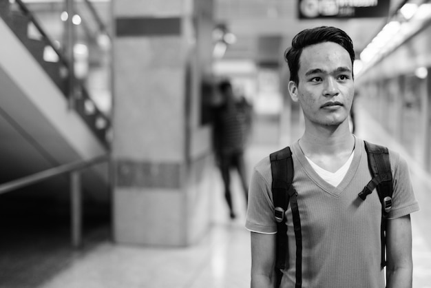 Ritratto di giovane uomo indiano bello alla stazione della metropolitana di Bangkok in bianco e nero