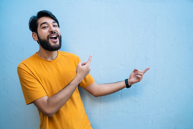 Ritratto di giovane uomo latino che punta e mostra qualcosa su sfondo blu.