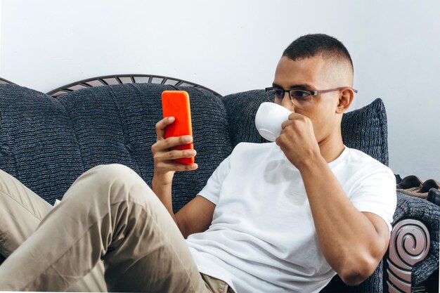 ritratto di giovane uomo latinoamericano bere in tazza guardando il telefono