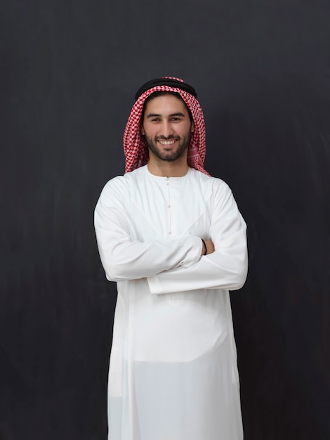 Ritratto di giovane uomo musulmano che indossa abiti tradizionali. Arabo felice in piedi davanti alla lavagna nera che rappresenta il concetto di Ramadan Kareem