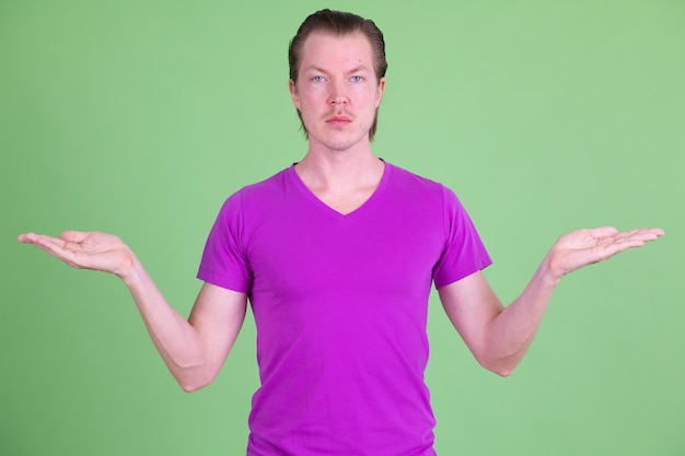 Ritratto di giovane uomo scandinavo bello che indossa la camicia viola contro la chiave di crominanza o la parete verde