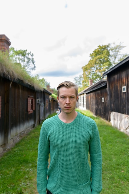 Ritratto di giovane uomo scandinavo bello nel mezzo di vecchi cottage in legno allineati