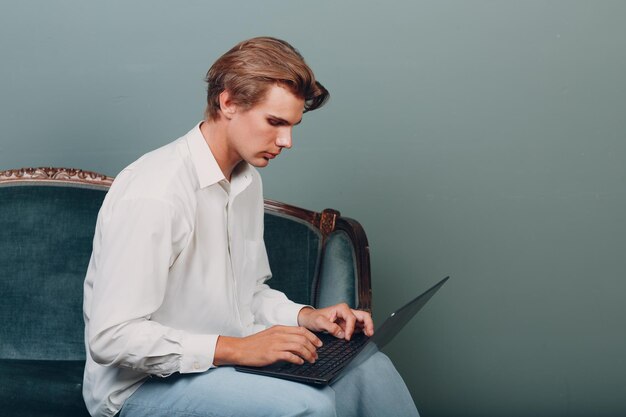 Ritratto di giovane uomo seduto con il computer portatile in studio