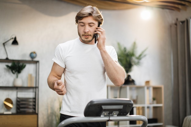 Ritratto di giovane uomo sportivo caucasico in abbigliamento sportivo che parla su smartphone