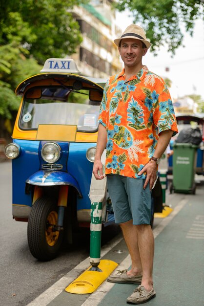 Ritratto di giovane uomo turistico bello con tuk tuk come trasporto pubblico locale nella città di Bangkok