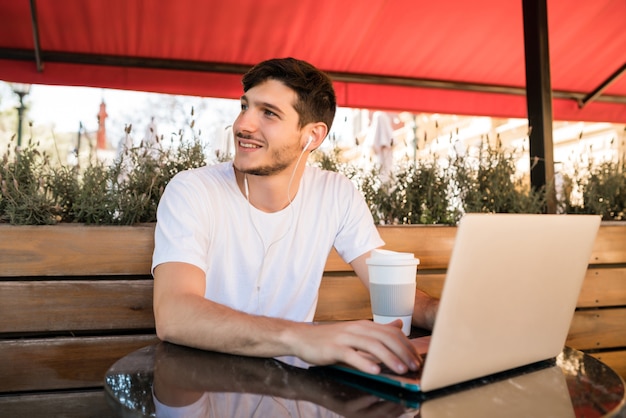 Ritratto di giovane uomo utilizzando il suo computer portatile mentre è seduto in una caffetteria. Concetto di tecnologia e stile di vita.