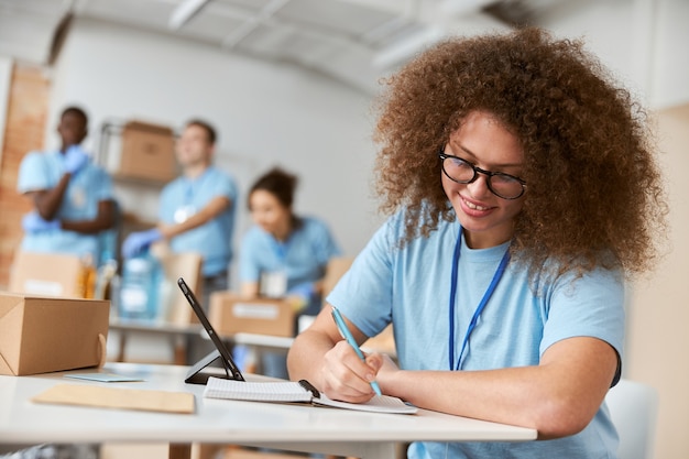 ritratto di giovane volontaria in uniforme blu che prende appunti mentre lavora al progetto di donazione