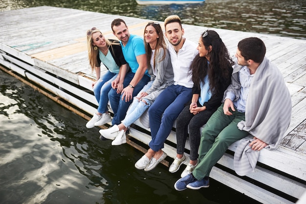 Ritratto di giovani amici felici seduti su un molo sul lago.
