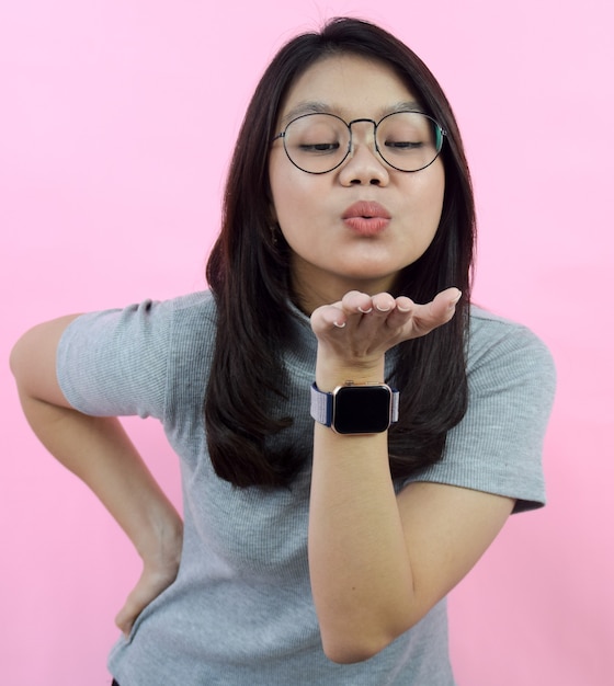 Ritratto di giovani belle donne asiatiche che usano la camicia grigia del collo di tutrtle che soffia un bacio con il rosa