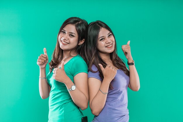 Ritratto di giovani ragazze gemelli bello affascinante allegro mentre mostra i pollici alla telecamera isolata su sfondo verde