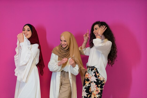 Ritratto di gruppo di belle donne musulmane due di loro in abito alla moda con hijab isolato su sfondo rosa che rappresenta la moda islam moderna e il concetto di ramadan kareem.