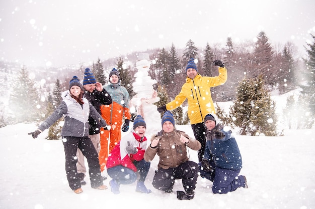 ritratto di gruppo di giovani uomini d'affari felici dopo una competizione in posa con un pupazzo di neve finito mentre si godono una giornata invernale innevata con fiocchi di neve intorno a loro durante un team building nella foresta di montagna